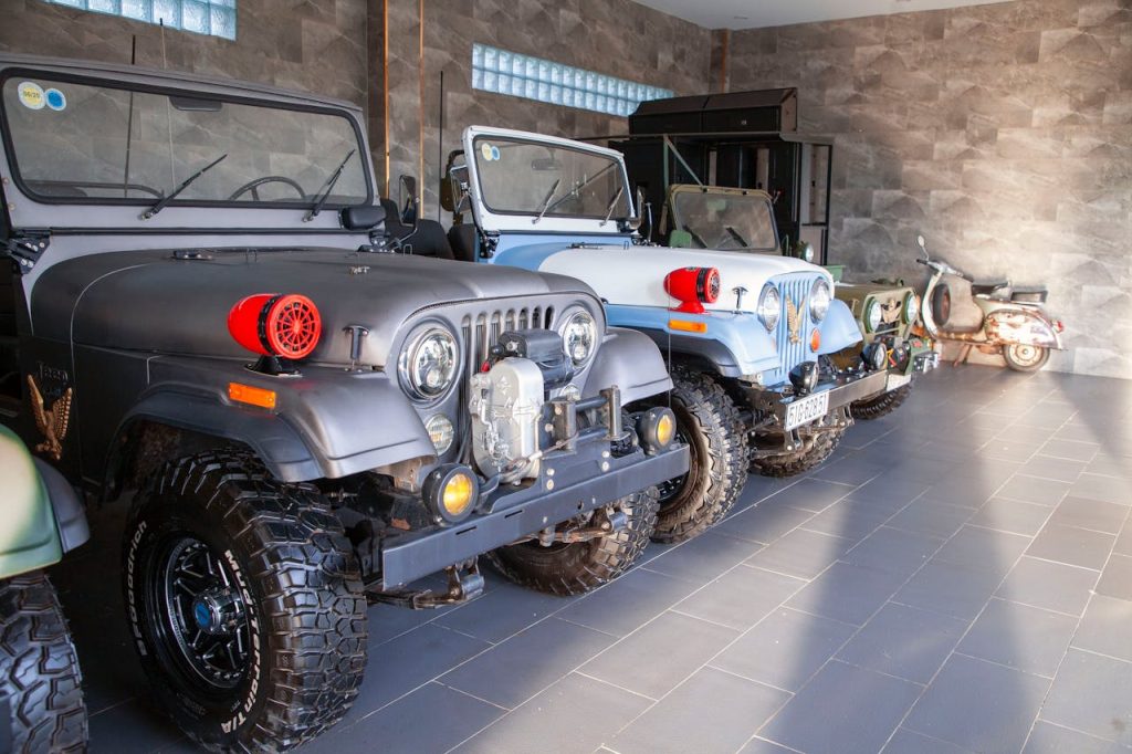 A collection of vintage Jeeps and a scooter inside a modern garage, showcasing classic automotive style.